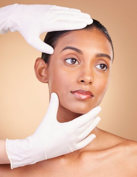 Beauty, plastic surgery and hands with face of Indian woman in studio for cosmetics, skincare and b.