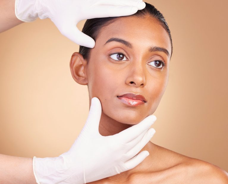 Beauty, plastic surgery and hands with face of Indian woman in studio for cosmetics, skincare and b.